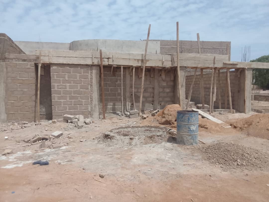 Chantier de construction de maison à Bamako montrant la maçonnerie en agglos, le coffrage en bois des poutres et des poteaux en béton en cours de réalisation au Mali.